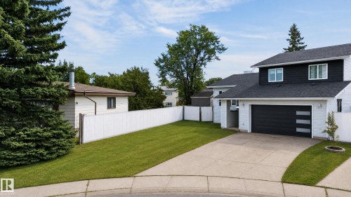 Contemporary two-story exterior with dark siding accents, attached garage with modern door, paved driveway, and a white picket fence - 17103 92 Street Nw, Edmonton, AB 