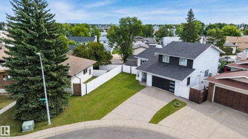 Exterior featuring a newly installed roof, a two-car garage with contemporary doors, a spacious paved driveway, a white privacy fence, and mature evergreen landscaping - 17103 92 Street Nw, Edmonton, AB 