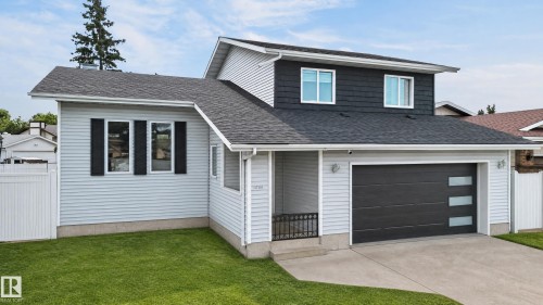 Two-story residence featuring light gray siding, dark gray shake siding, a dark gray garage door with frosted glass panels, a concrete driveway, and a white fence - 17103 92 Street Nw, Edmonton, AB 