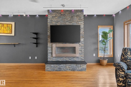 Stacked stone fireplace with a raised hearth, wood-finish flooring, and track lighting - 17103 92 Street Nw, Edmonton, AB 