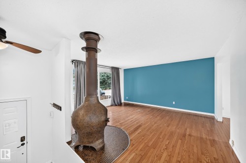 Wood-finish flooring, accent wall, ceiling fan, and a floor-to-ceiling fireplace with a tiled base - 11007 37 Avenue Nw, Edmonton, AB 