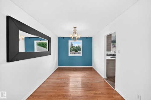 Wood-finish flooring throughout, complemented by a modern chandelier and a window providing natural light - 11007 37 Avenue Nw, Edmonton, AB 