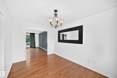 Hardwood-style flooring throughout, an overhead chandelier with frosted glass shades, and a framed wall mirror - 11007 37 Avenue Nw, Edmonton, AB 