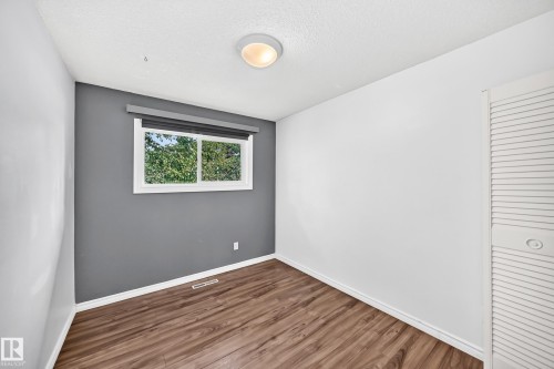 Wood-finish flooring, white trim, a built-in closet with louvered doors, and a window with a roller shade - 11007 37 Avenue Nw, Edmonton, AB 
