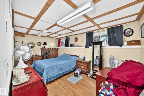 Wood-finish flooring, two windows with dark curtains, and a grid-patterned ceiling with exposed wood beams - 11007 37 Avenue Nw, Edmonton, AB 