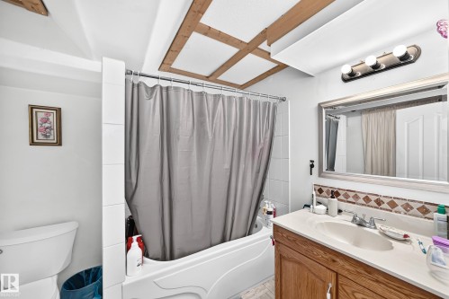 Tub-shower combination with white tile surround, wood-finish vanity with countertop, and framed mirror - 11007 37 Avenue Nw, Edmonton, AB 