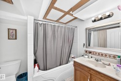 Tub-shower combination with white tile surround, wood-finish vanity with countertop, and framed mirror - 