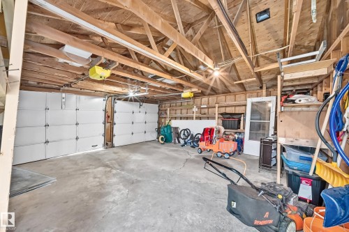 Spacious garage featuring a concrete floor, exposed wood beam ceiling, two sectional garage doors, and built-in shelving - 11007 37 Avenue Nw, Edmonton, AB 