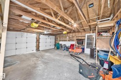 Spacious garage featuring a concrete floor, exposed wood beam ceiling, two sectional garage doors, and built-in shelving - 