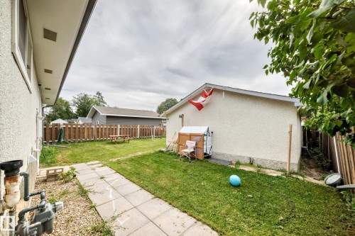 Expansive grassy backyard featuring a paved pathway, a wood privacy fence, and mature trees - 11007 37 Avenue Nw, Edmonton, AB 