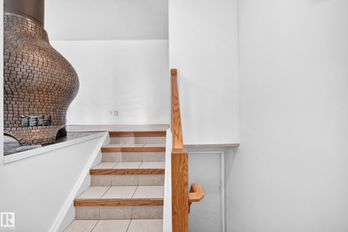 Stone brick fireplace with a dark hearth, wood-finish handrail, and tiled stairs with wood-finish risers - 11007 37 Avenue Nw, Edmonton, AB 
