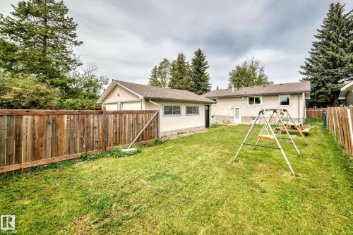 Expansive backyard featuring a lush lawn, privacy fencing, detached garage, and a rear entrance to the residence - 11007 37 Avenue Nw, Edmonton, AB 
