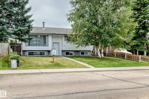 Split-level residence featuring a front lawn with established landscaping, a concrete sidewalk leading to the front entry, and a partial wooden fence - 11007 37 Avenue Nw, Edmonton, AB 