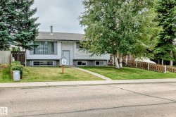 Split-level residence featuring a front lawn with established landscaping, a concrete sidewalk leading to the front entry, and a partial wooden fence - 