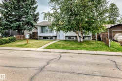 White siding exterior with a contrasting gray trim, front yard with a manicured lawn, concrete pathway, and mature trees - 