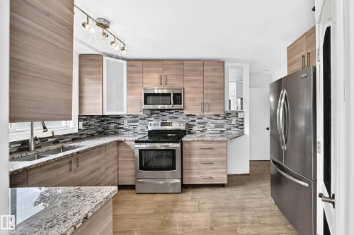 Stainless steel appliances, wood-finish cabinetry, granite countertops, mosaic tile backsplash, and tile flooring - 11007 37 Avenue Nw, Edmonton, AB 