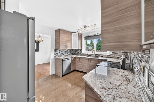 Kitchen featuring wood-finish cabinetry, stainless steel appliances, granite-style countertops, mosaic tile backsplash, and tile flooring - 11007 37 Avenue Nw, Edmonton, AB 