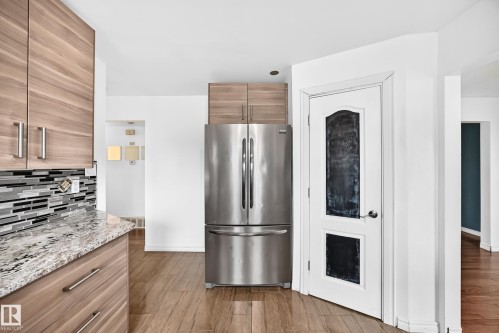Wood-finish cabinetry, stainless steel refrigerator, patterned tile backsplash, natural stone countertop, and wood-finish flooring - 11007 37 Avenue Nw, Edmonton, AB 