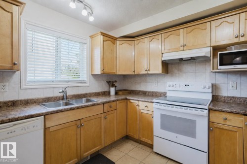Kitchen featuring light wood cabinetry, stone-look countertops, and a tile backsplash - 10332 161 Street Nw, Edmonton, AB 
