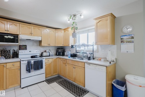 U-shaped kitchen featuring wood cabinetry, white tile flooring, white appliances, and a window above the sink - 10334 161 Street Nw, Edmonton, AB 
