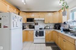 U-shaped kitchen featuring wood-finish cabinetry, tile flooring, white appliances, a double basin stainless steel sink, and a tiled backsplash - 