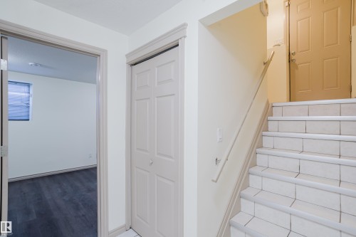 Tile-finished stairs with a handrail, bi-fold closet doors, and wood-finish flooring in an adjacent room - 10334 161 Street Nw, Edmonton, AB 