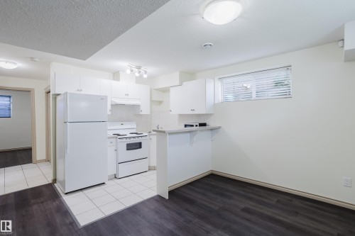 Kitchen featuring white cabinetry, white appliances, track lighting, and a breakfast bar - 10334 161 Street Nw, Edmonton, AB 