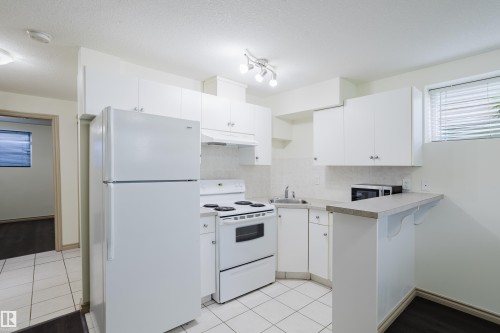 Kitchen featuring white appliances, white cabinetry, light-toned countertops, and tile flooring - 10334 161 Street Nw, Edmonton, AB 