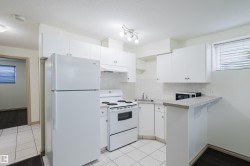 Kitchen featuring white appliances, white cabinetry, light-toned countertops, and tile flooring - 