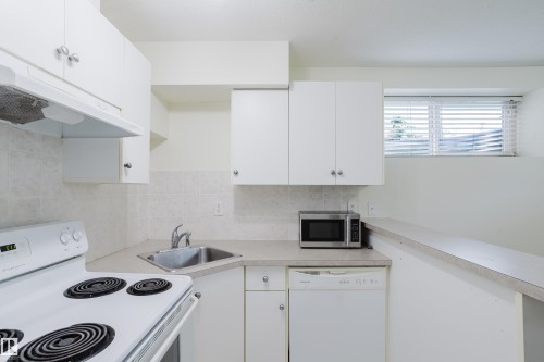 White cabinetry and countertop space with a stainless steel sink, tile backsplash, and built-in dishwasher - 10334 161 Street Nw, Edmonton, AB 