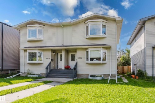 Duplex exterior featuring light-colored siding, multiple bay windows, front entries with multi-pane doors, and concrete walkways - 10334 161 Street Nw, Edmonton, AB 
