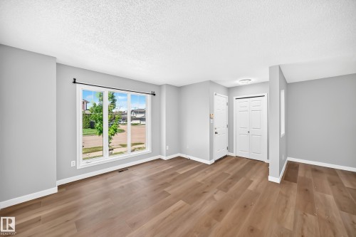 Bright interior space featuring a large three-panel window, wood-finish flooring, light gray walls, white trim, and a white entry door - 203 84 Street Sw, Edmonton, AB - Indoor Photo Showing Other Room