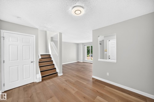 Open-concept living area featuring wood-finish flooring, a contemporary ceiling light fixture, and a staircase with contrasting risers - 203 84 Street Sw, Edmonton, AB - Indoor Photo Showing Other Room