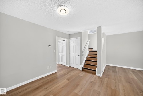 Expansive room featuring wood-finish flooring, light grey painted walls, white trim, and a contemporary ceiling light fixture - 203 84 Street Sw, Edmonton, AB - Indoor Photo Showing Other Room