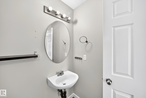Wall-mounted sink with a chrome faucet, illuminated by a four-bulb vanity light fixture - 203 84 Street Sw, Edmonton, AB - Indoor Photo Showing Bathroom