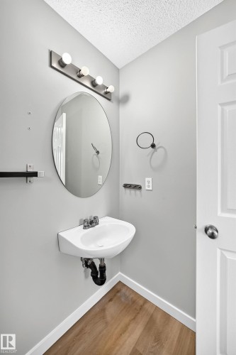 Pedestal sink with chrome faucet, complemented by an oval mirror and a five-bulb vanity light fixture - 203 84 Street Sw, Edmonton, AB - Indoor Photo Showing Bathroom