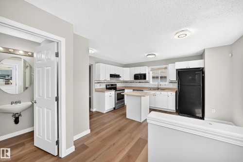 Open-concept kitchen featuring white cabinetry, light countertops, subway tile backsplash, and wood-finish flooring - 203 84 Street Sw, Edmonton, AB - Indoor Photo Showing Kitchen