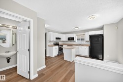 Open-concept kitchen featuring white cabinetry, light countertops, subway tile backsplash, and wood-finish flooring - 