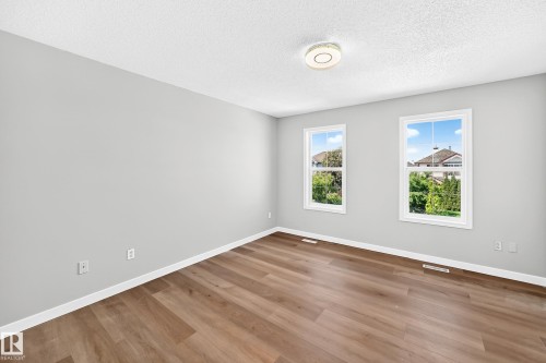 Bright room featuring two double-hung windows with white trim, wood-finish flooring, light gray walls, and a ceiling-mounted light fixture - 203 84 Street Sw, Edmonton, AB - Indoor Photo Showing Other Room