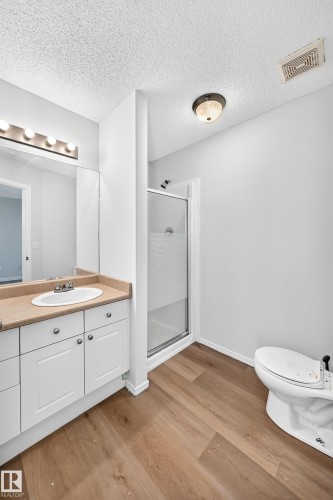 Bathroom featuring wood-finish flooring, a white single-sink vanity with a light-colored countertop, a chrome faucet, and a large wall-mounted mirror - 203 84 Street Sw, Edmonton, AB - Indoor Photo Showing Bathroom