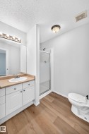 Bathroom featuring wood-finish flooring, a white single-sink vanity with a light-colored countertop, a chrome faucet, and a large wall-mounted mirror - 