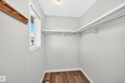 Walk-in closet with wood-finish flooring, light gray wall paint, and white trim - 