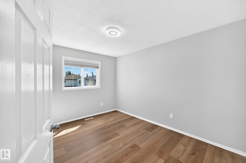 Neutral gray walls with white trim, wood-finish flooring, and a single window with a white frame - 203 84 Street Sw, Edmonton, AB - Indoor Photo Showing Other Room