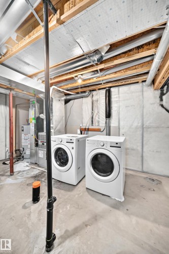 Utility area featuring a front-loading washer and dryer set, exposed ceiling joists, and concrete flooring - 203 84 Street Sw, Edmonton, AB - Indoor Photo Showing Laundry Room