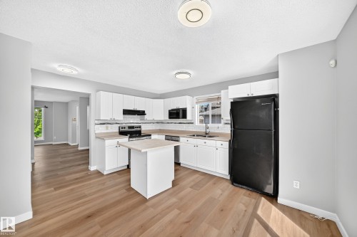 Kitchen featuring white shaker cabinetry, black appliances, light wood-finish flooring, and a white tile backsplash - 203 84 Street Sw, Edmonton, AB - Indoor Photo Showing Kitchen