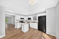 Kitchen featuring white shaker cabinetry, black appliances, light wood-finish flooring, and a white tile backsplash - 