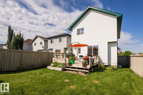 Expansive grassy yard featuring a multi-level wood deck, a sliding glass door for patio access, and a perimeter wood fence - 203 84 Street Sw, Edmonton, AB - Outdoor With Deck Patio Veranda
