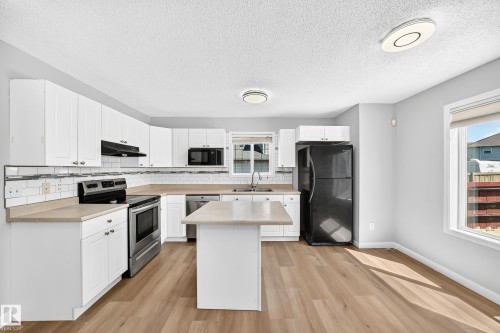 Kitchen featuring white cabinetry, wood-finish flooring, a central island, stainless steel appliances, and a subway tile backsplash - 203 84 Street Sw, Edmonton, AB - Indoor Photo Showing Kitchen With Double Sink With Upgraded Kitchen