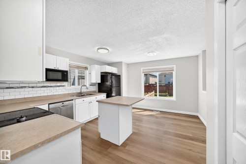 Bright kitchen featuring white cabinetry, light-toned countertops, a subway tile backsplash, and stainless steel appliances - 203 84 Street Sw, Edmonton, AB - Indoor Photo Showing Kitchen