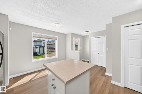 Central island with countertop, wood-finish flooring, light grey wall paint, modern ceiling lighting, and white baseboards - 203 84 Street Sw, Edmonton, AB - Indoor Photo Showing Kitchen